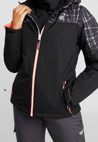 Schwarze Zip-Jacke mit orangefarbenen Akzenten, einem karierten Muster auf den Schultern und Reißverschlusstaschen. Hergestellt aus einem glatten, strapazierfähigen Material.