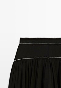 Gonna nera con ampia fascia in vita e cuciture a contrasto bianche nella parte superiore e centrale, con tessuto arricciato sotto la cucitura.