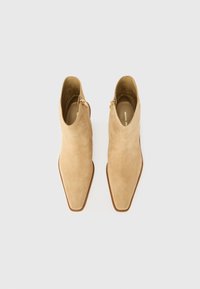 Stivaletti alla caviglia in suede color tan con punta a forma appuntita, chiusura con zip laterale e suola beige liscia. Parte superiore testurizzata con finitura senza cuciture.