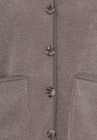 Veste en polaire taupe texturée avec quatre boutons marbrés et deux poches avant, montrant les détails des boutons et des poches.