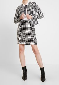 Conjunto de blazer y falda de patrón de espiga en blanco y negro, que presenta un diseño ajustado y textura. Llevado con una blusa blanca y botines negros.