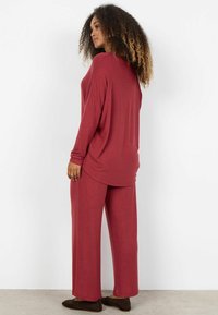 Súprava na voľný čas v gaštanovej farbe s voľným strihom, dlhým rukávom a nohavicami s širokými nohavicami. Mäkká textúra, zaoblený lem a minimalistický dizajn.