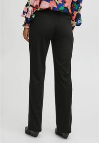 Black, stretchy trousers with a smooth texture. Features a relaxed fit and slim leg design. Worn with a multicolored floral blouse.