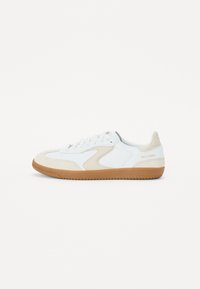 Hvite sneakers med brune detaljer, materialer i semsket skinn og glatt lær, rund tå, flat såle i gummigummi, og logo på hælen.