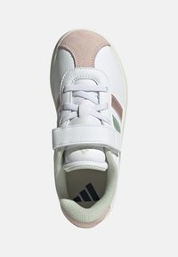 Baskets blanches de sport avec un accent en daim rose, des détails verts et une sangle ajustable. Doublure texturée avec trois rayures noires sur la semelle.