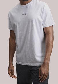 Bílá bavlněná tričko s kulatým výstřihem a krátkými rukávy. Černé logo "HALO" na hrudi. Hladká textura a uvolněný střih.
