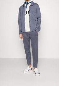 Casual outfit featuring a blue sweatshirt jacket, white graphic t-shirt, matching blue pants, and white slip-on shoes with red accents.