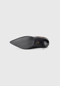 Chaussure à talon haut noire avec bout pointu, surface texturée et accent en chaîne dorée. Présente un logo sur la semelle intérieure et un talon lisse.