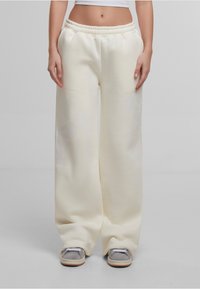 Pantalons de survêtement larges couleur crème avec une taille élastique, fabriqués en tissu doux, offrant un léger brillant et sans motifs visibles.