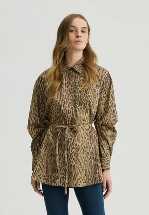 Chemise imprimée léopard en beige et marron, avec un col à bouton, des manches longues, une taille nouée et une poche décorative avec des embellissements.