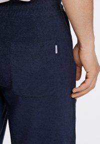 Marinblå frottébyxor med en bakficka och en liten märkesskylt. Tyget har en mjuk, texturerad yta.