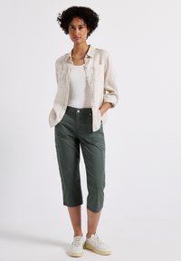 Ljusbeige linneskjorta med knappar, vit linne-topp, olivgröna korta cargobyxor med fickor och vita sneakers. Släta texturer och avslappnad passform.