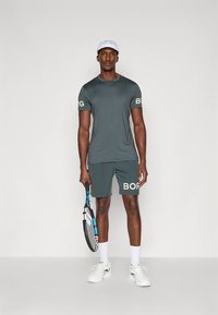Gray athletic t-shirt and shorts, both featuring white "BORG" text. Subject holds a tennis racket, wearing a white cap and shoes.