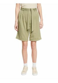 Shorts verts ajustés avec une taille haute, des plis et une ceinture à nouer. Dotés d'ourlets retournés et d'un tissu léger. Portés avec des baskets légères.