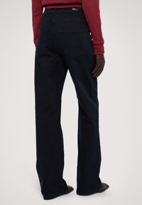 Tmavě modré džíny s vysokým pasem a širokým střihem. Mají dvě zadní kapsy a jemné švy, kombinované s červeným svetr a rukavicemi.