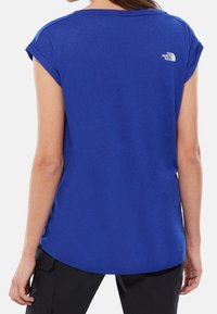 Blå kortärmad skjorta gjord av ett slätt tyg, med rundad nederkant och en liten vit logotyp på den övre ryggen.