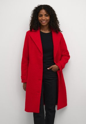 Red, textured long coat with a wide collar, single-breasted design, and flap pockets; worn over a black top and paired with black pants.