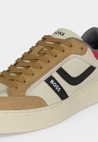 Baskets basses avec superpositions en daim couleur tan, panneaux en cuir beige, bande noire avec logo "BOSS" et lacets marron sur une semelle blanche texturée.