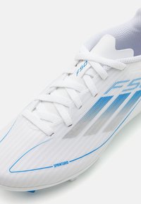 Scarpini da calcio bianchi con accenti blu e superiore testurizzato a righe. Presentano lacci e il marchio "F50". Design leggero con una forma aerodinamica.