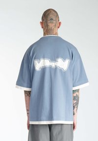Lysblå oversized t-shirt med en hvid accentfarve ved kraven og manchetterne, med et kontrasterende grafik på ryggen i hvid og grå nuancer.