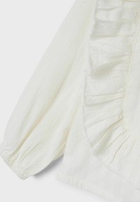 Blusa blanca con tejido texturizado y un patrón de diamantes, con detalles de volantes a lo largo de las costuras y mangas abullonadas fruncidas.