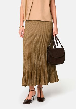 Metallic plissierter Rock in Gold mit einem ausladenden Saum, kombiniert mit einer braunen Wildledertasche und braunen Absatzschuhen. Das Oberteil ist beige und locker sitzend.