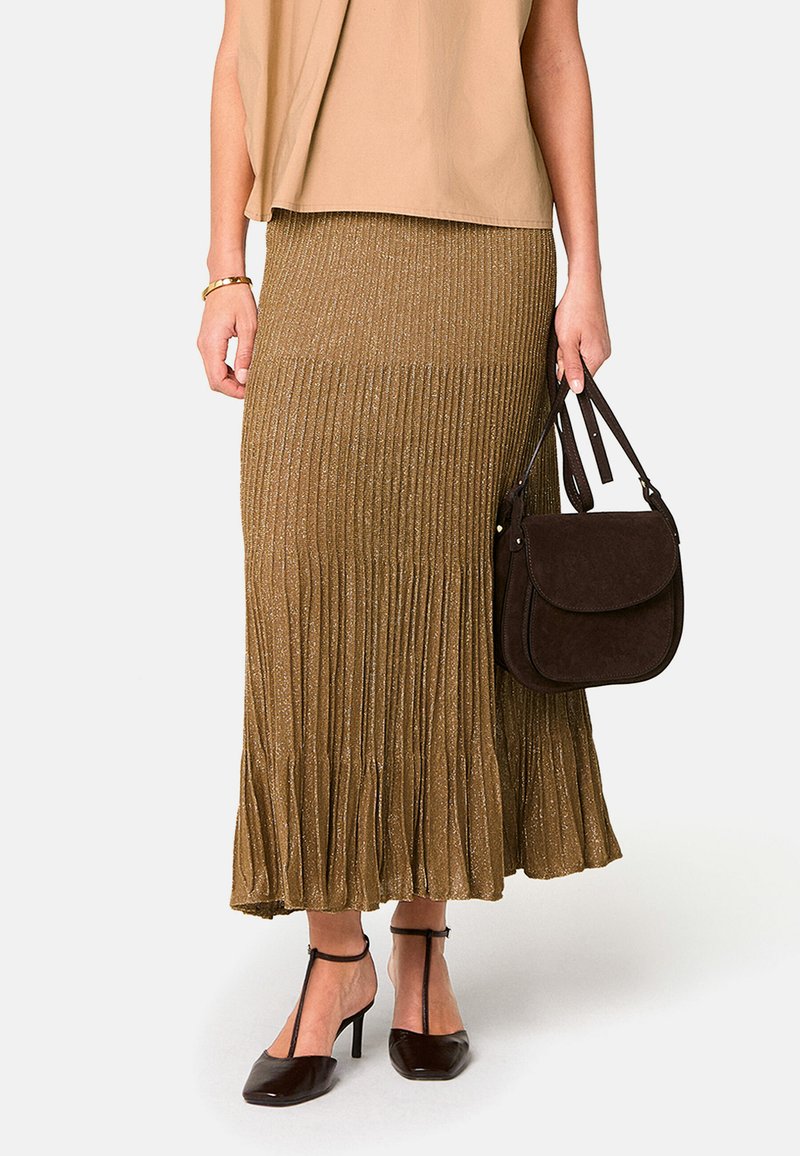 Jupe plissée métallique dorée avec un ourlet évasé, associée à un sac en daim marron et des chaussures à talons marron. Le haut est beige et ample.