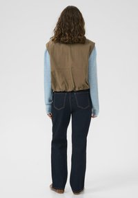 Khaki mellény világoskék kötött pulóver fölött, sötétkék farmernadrággal párosítva. Egyenes szárú, hátsó zsebfelvarrással.