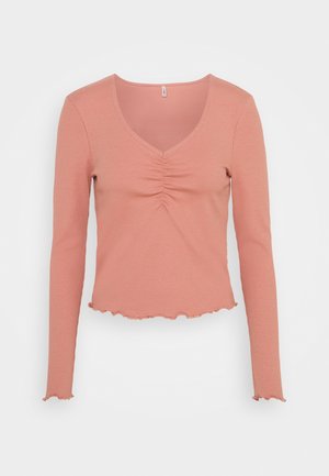 Haut rose à manches longues côtelé avec encolure en V, plissé au centre devant et bord ondulé aux manches et en bas.