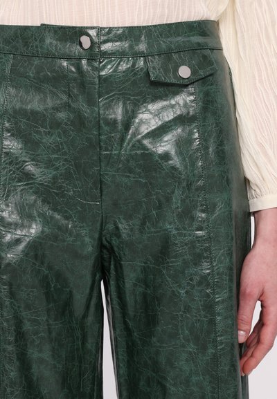 Groene neplederen broek met een glanzende textuur, hoge taille, knoopsluiting aan de voorkant en zijzakken met zichtbare stikdetails.
