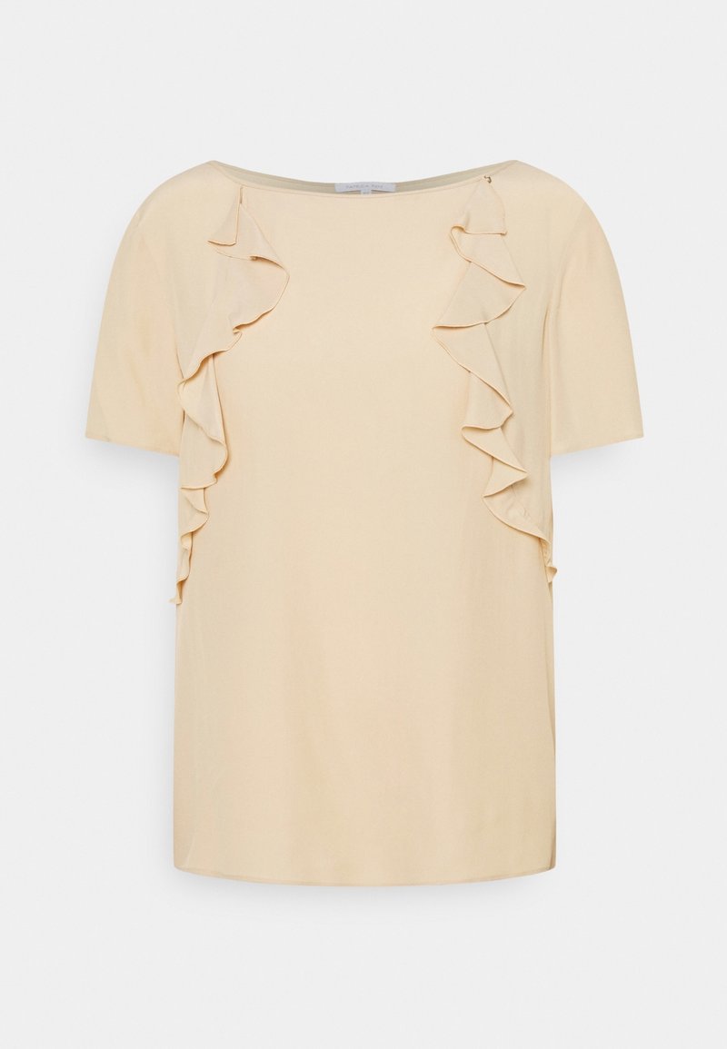 Blouse courte à manches courtes couleur crème avec encolure bateau et détails de volants verticaux sur les côtés avant, sur un fond uni.
