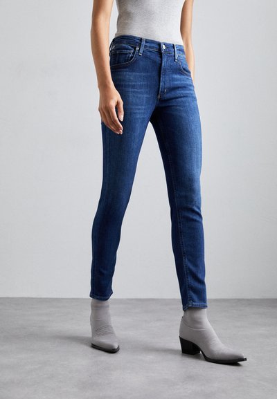 Blugi skinny din denim albastru cu talie medie, cinci buzunare și un croi slim. Asortați cu ghete cu șosete gri și un top gri ajustat.