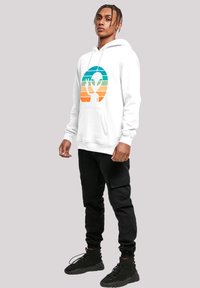 White hoodie featuring a multicolored graphic of an alien with a peace sign, paired with black cargo pants and black sneakers.