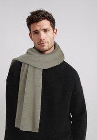 Écharpe gris en maille côtelée drapée sur un pull noir texturé, présentant un design doux et épais ainsi qu'une palette de couleurs neutres.