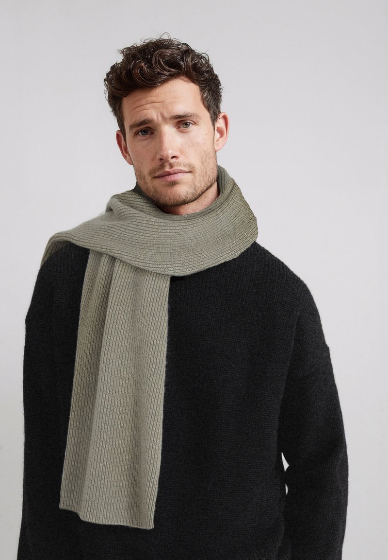 Écharpe gris en maille côtelée drapée sur un pull noir texturé, présentant un design doux et épais ainsi qu'une palette de couleurs neutres.