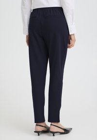 Pantaloni bleumarin cu talie elastică, două buzunare în spate, design cu croială conică și textură fină a țesăturii, asortați cu pantofi negri cu barete la călcâi.
