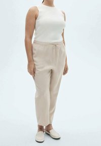 Beige elastische taille broek en een witte mouwloze top. De stof lijkt zacht, met gladde texturen. Eenvoudig ontwerp en neutrale kleuren.