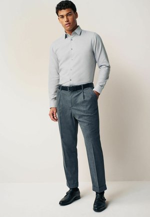 Jasnoszara koszula z długim rękawem, zapinana na guziki, w połączeniu z szarymi spodniami w kratkę i czarnymi skórzanymi butami. Slim fit, gładka tekstura materiału.