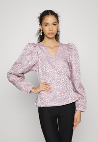 Blusa com padrão floral em lavanda suave, com mangas bufantes, decote em V e punhos elásticos. Combinada com calças pretas ajustadas.