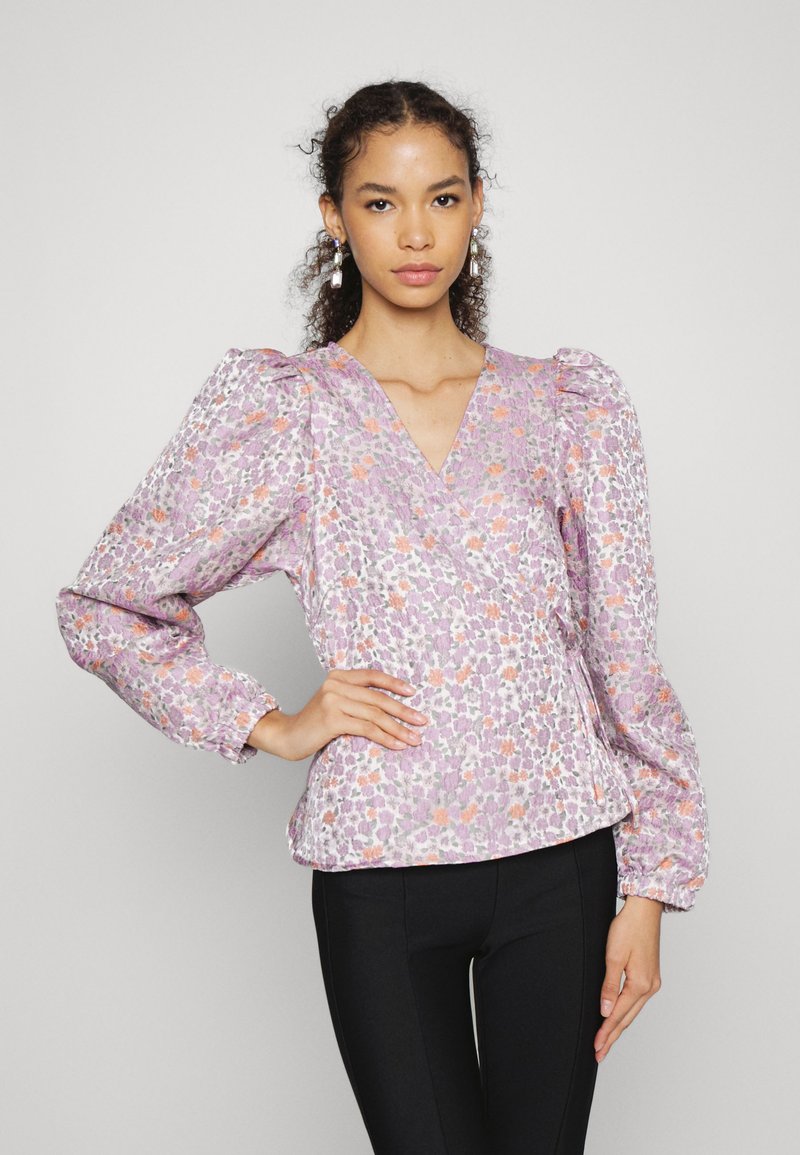 Blusa com padrão floral em lavanda suave, com mangas bufantes, decote em V e punhos elásticos. Combinada com calças pretas ajustadas.