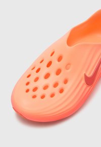 Pantof Nike slip-on în portocaliu aprins, cu striații texturate, găuri de ventilație și un logo roșu contrastant pe lateral. Material neted și ușor.