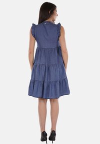 Abito in denim con maniche a sbuffo, design a strati e orlo fino al ginocchio. Colore: blu scuro. La vista posteriore mostra una chiusura con bottoni al collo.