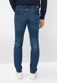 Dunkelblaue Jeans mit schlanker Passform, ausgestattet mit zwei Gesäßtaschen und Kontrastnähten, kombiniert mit weißen Sneakers.