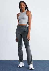 Gray cropped tank top with a subtle logo, paired with dark green corduroy flared pants, complemented by white athletic shoes.