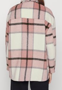 Flanellipaita, jossa on vaaleanpunainen, valkoinen ja musta ruutukuvio. Pehmeä koostumus, nappikaulus ja sivuhaarat helmassa.