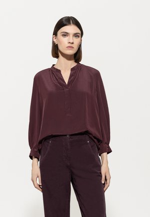 Burgunderfarbene Seidenbluse mit V-Ausschnitt, langen Ärmeln und lässiger Passform, kombiniert mit passenden dunklen Hosen. Sanfte Textur, minimale Details.