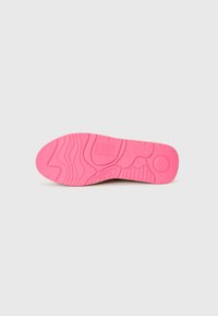 Semelle de chaussure en caoutchouc rose avec des motifs texturés, un logo et des détails de taille, sur fond blanc uni.