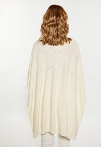 Poncho din tricot de fildeș cu un model în zig-zag, cu părți laterale deschise și tiv canelat. Textură moale, se drapează liber pentru o ajustare relaxată.