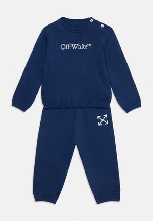 Тъмносиньо плетено дълъг ръкав горнище с текст "Off-White" и подходящ панталон с бял логотип с форма на стрелка на лявото бедро. Копчета на раменете на горнището.