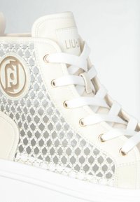 Hoge sneakers van crèmekleurig leer met een metalen gaas aan de zijkant, witte veters en gouden accenten. Heeft een gestructureerde buitenkant en een witte zool.